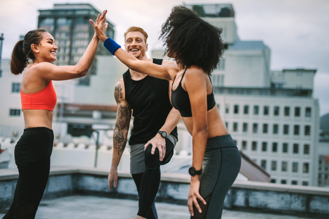 Three people in workout clothes, two are high-fiving; how to get clients as a new personal trainer
